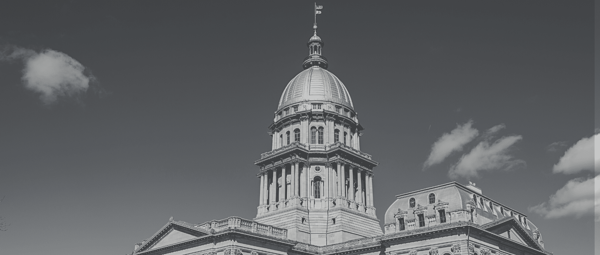 Black and white image of the Illinois State Capitol dome in Springfield, Illinois, against a partly cloudy sky.